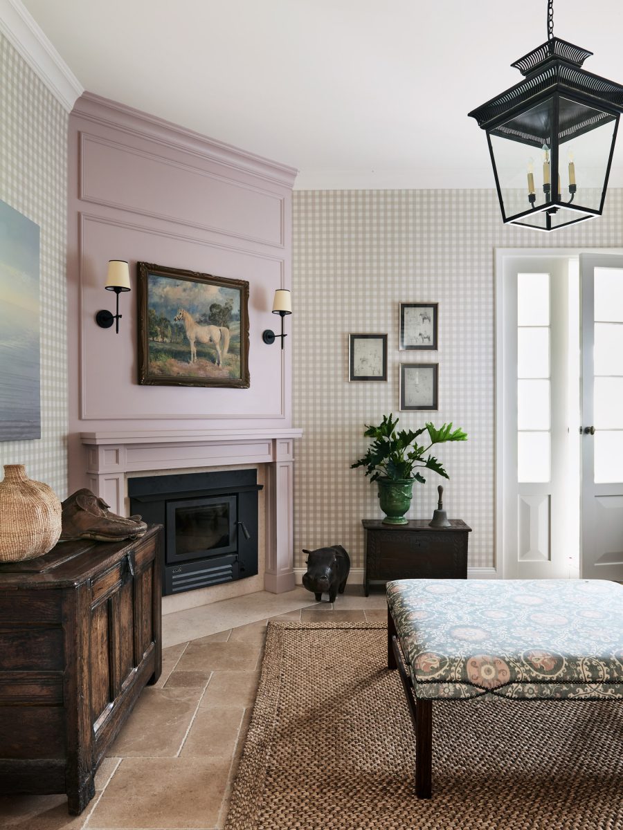 A Library Featuring A Dusty Rose Painted Fireplace Mantel With A Black Insert, Schumacher Checked Wallpaper, A Large Black Lantern Pendant Light, And A Sisal Rug.