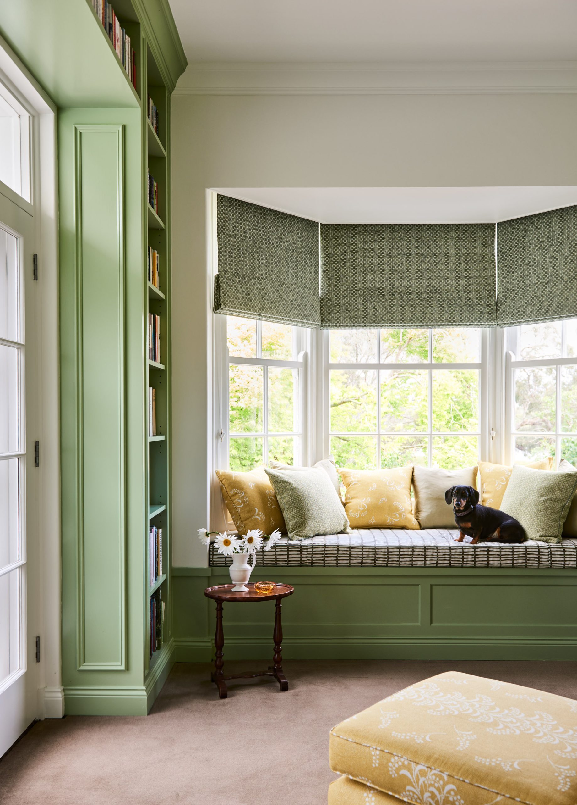 A Built-In Green Window Seat With Yellow Cushions And A Dachshund, Flanked By Floor-To-Ceiling Green Bookshelves.