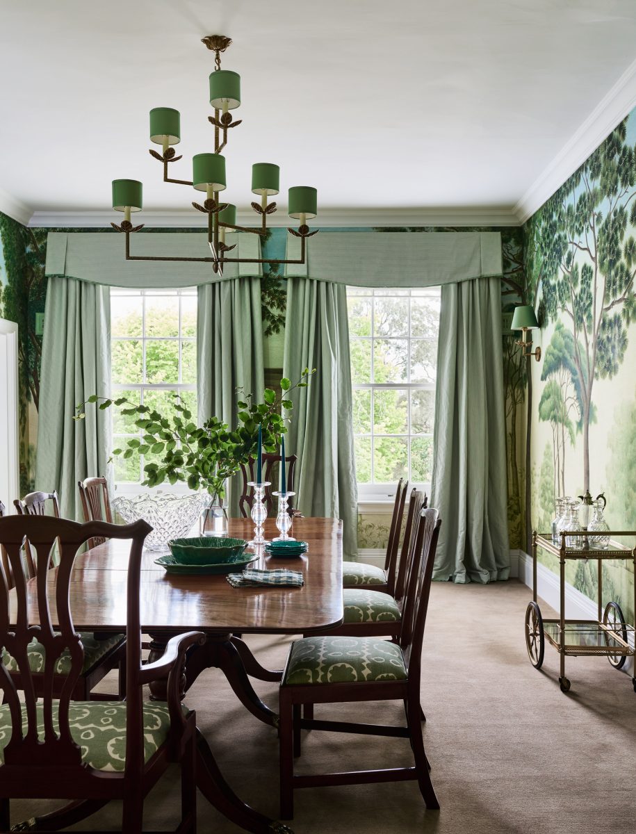 A Formal Dining Room Featuring Green Iksel Italian Panoramic Wallpaper, A Large Timber Table, And A Leaf-Themed Chandelier.