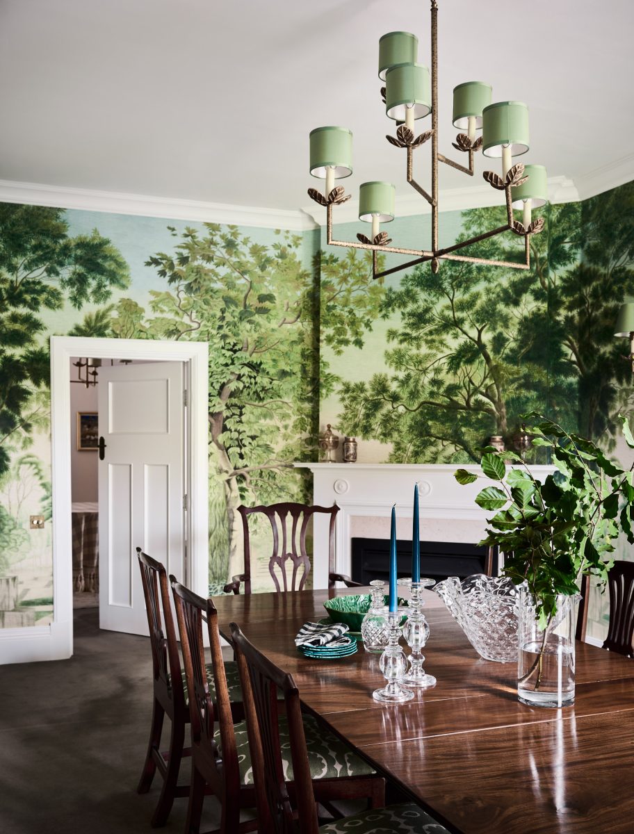 A Formal Dining Room Featuring Full-Wall Iksel Italian Panoramic Wallpaper, A White Mantelpiece, And A Bronze Vaughan Colombier Chandelier.