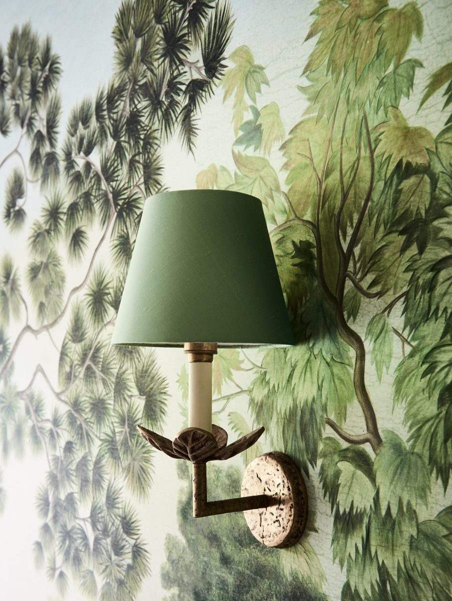 A Bronze Leaf-Motif Wall Sconce With A Green Shade, Mounted On A Panoramic Forest Wallpaper In The Casterton Homestead.