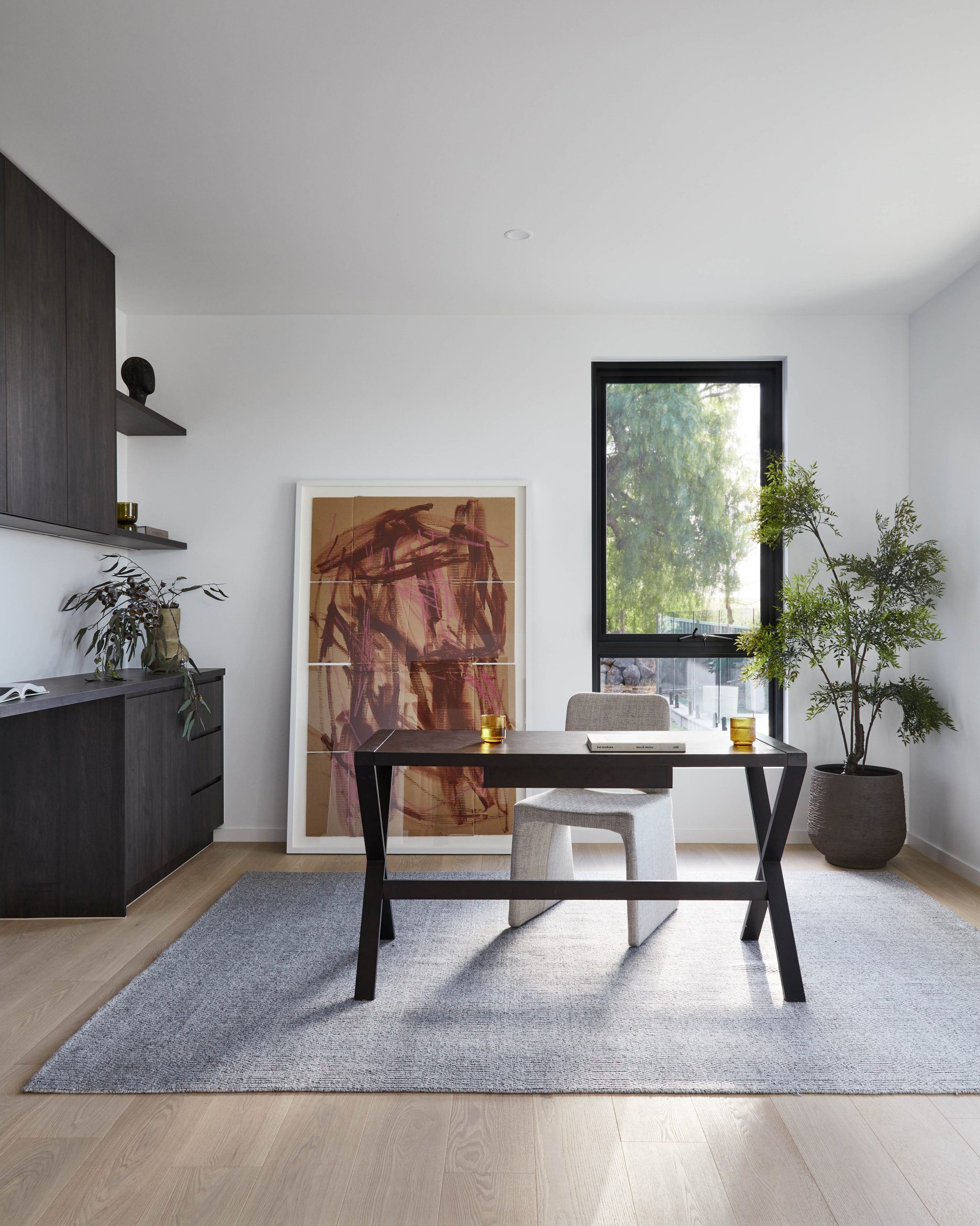 Timber Home Office Desk Beneath Framed Artwork And A Potted Plant