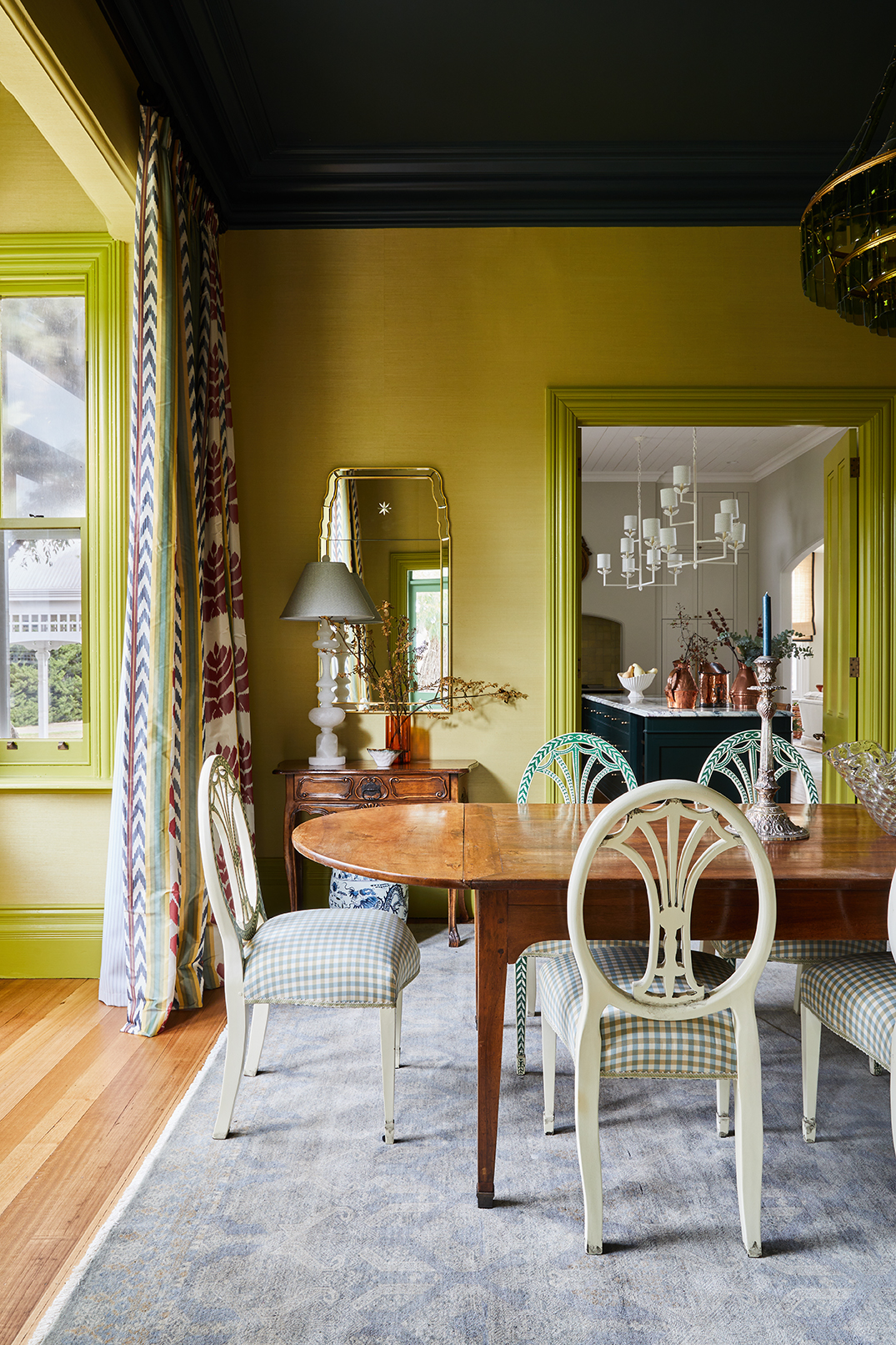 Tullynagee Dining Room Featuring Radiant Yellow Walls And Timber Table, Looking Through A Green Doorway Into The White Marble Kitchen.