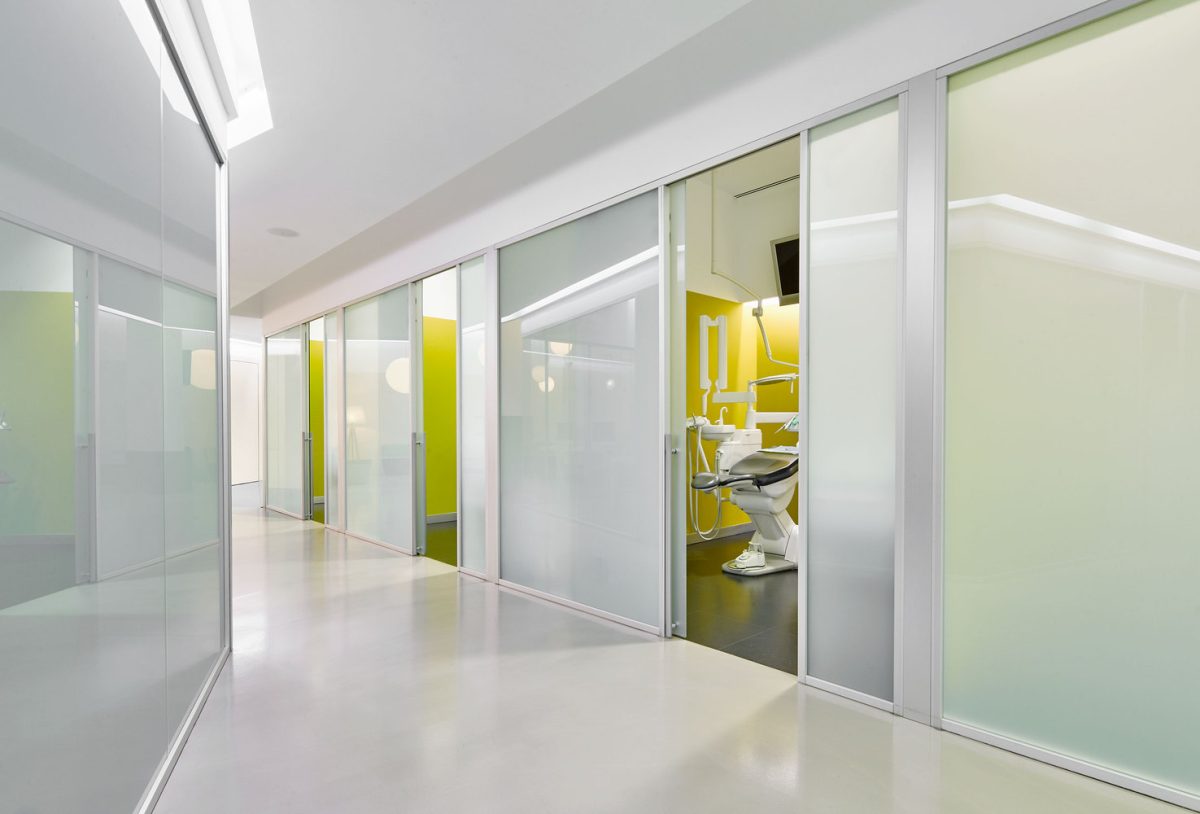 A Sterile Medical Clinic Corridor Featuring Frosted Glass Partitioning, Integrated Cove Lighting, And High-Performance Hygiene-Grade Flooring.