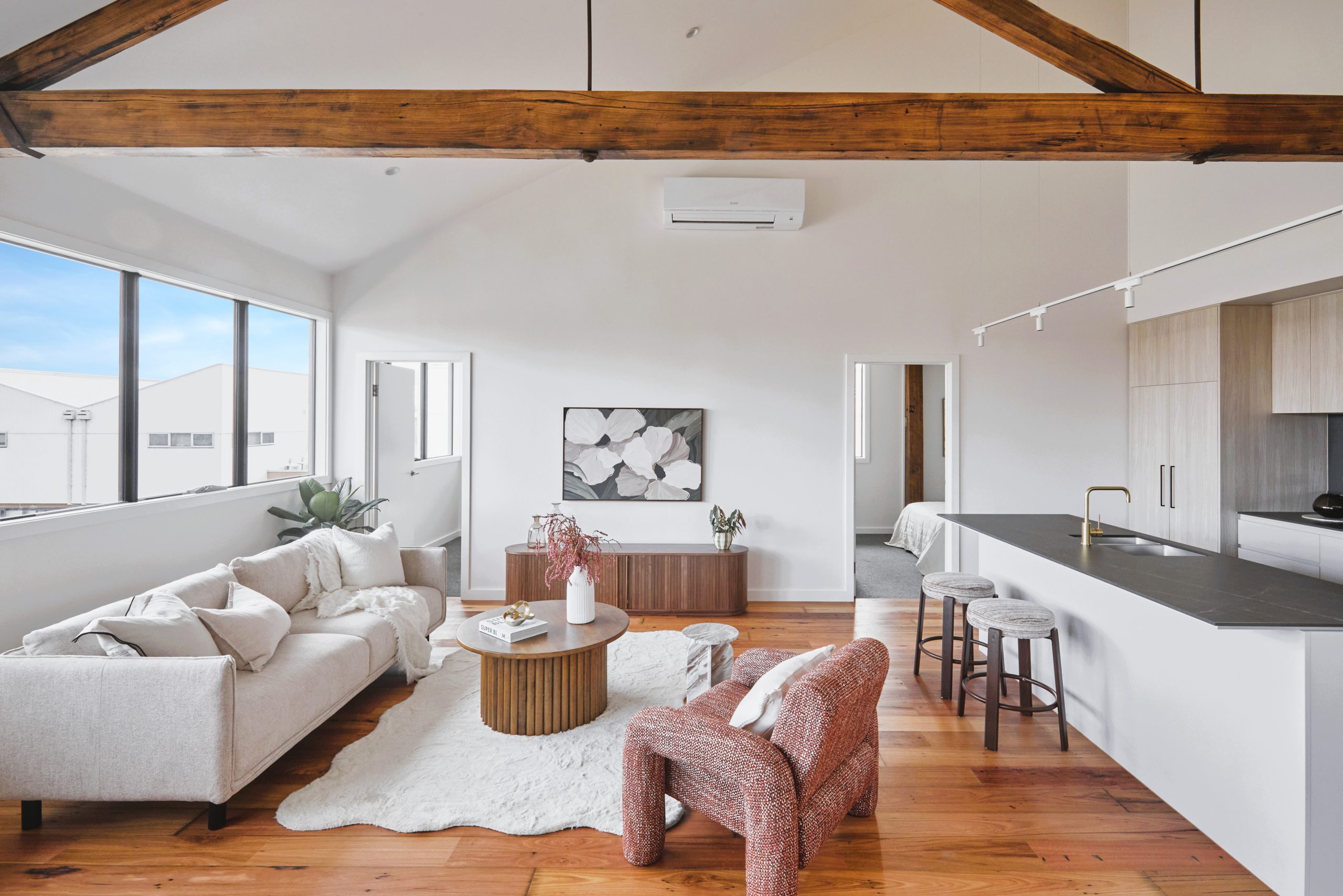 Open-Plan Apartment Interior Framing Preserved 1920S Timber Roof Trusses Over A Modern Living Area, Timber Floorboards, And Kitchen Island.