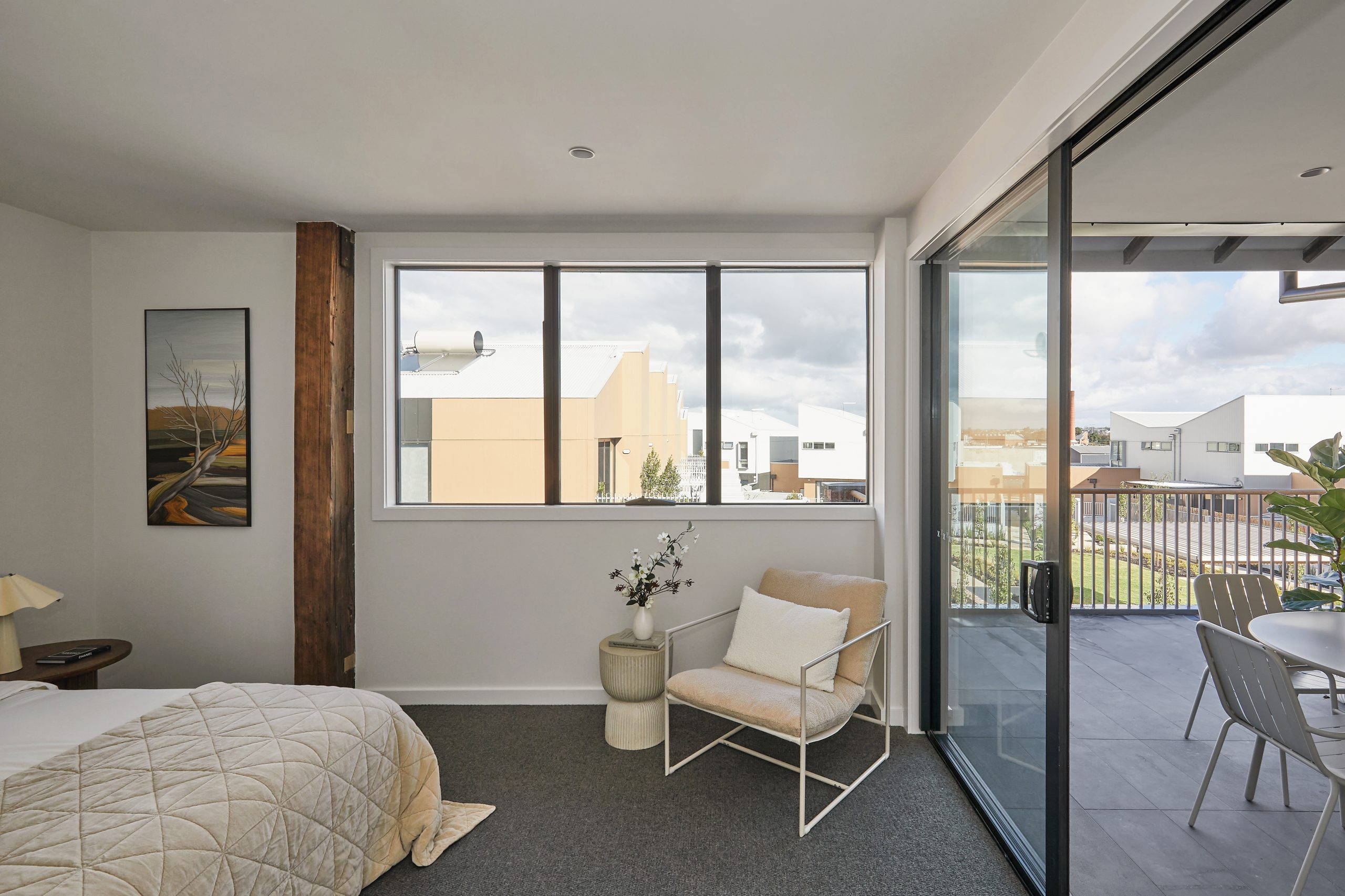 Apartment Bedroom Interior Featuring A Preserved Timber Column, Large Window To Residential Views, And Sliding Door Access To A Private Balcony.