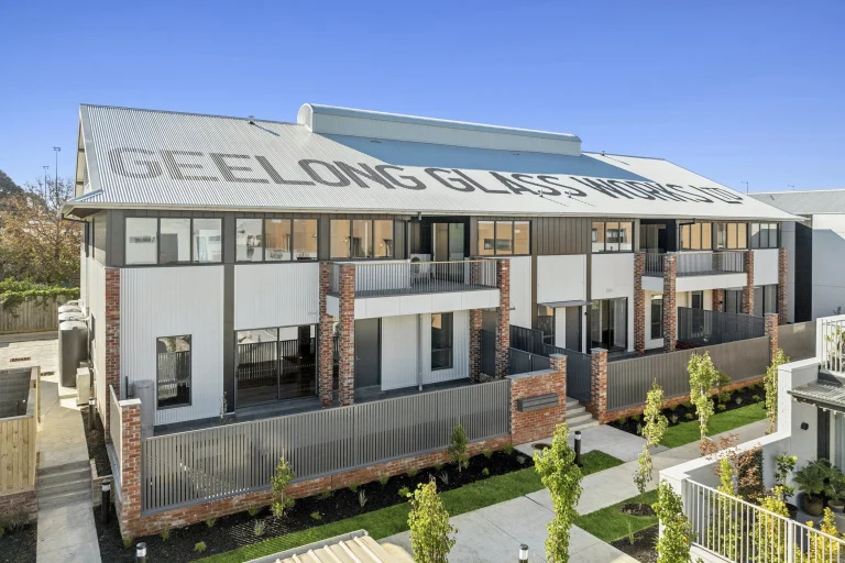 Elevated View Of Heritage Glassworks Conversion With Metal Envelope Cladding, Structural Recycled Brick Piers, And Balconies Over Terraces.