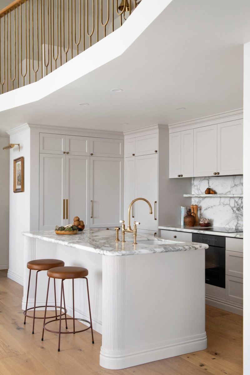 Marble Kitchen Island With Brass Tapware Beneath The Curved Mezzanine Staircase In The Award-Winning Carlton Renovation By Fox Building Group.